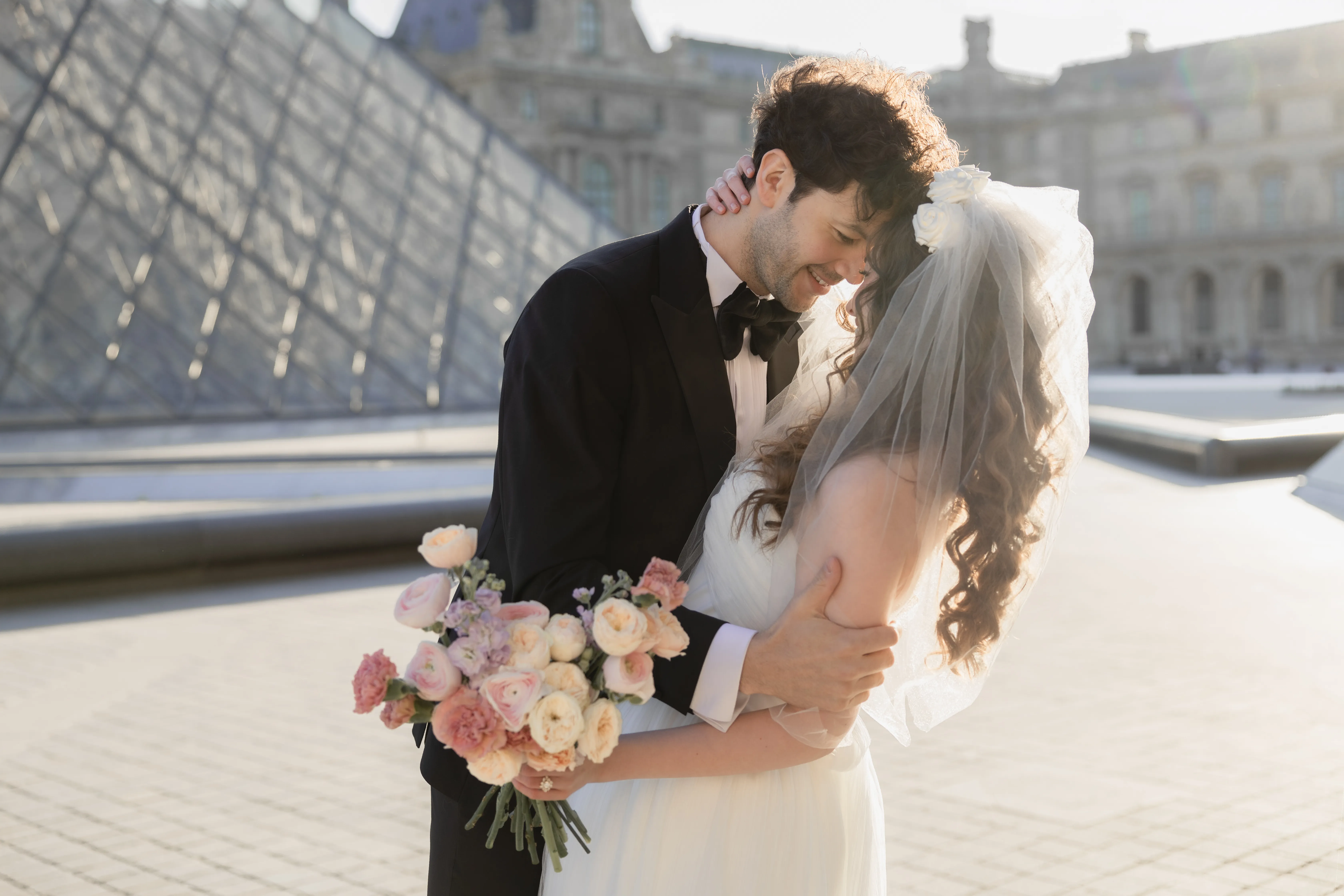 Newlyweds embracing in the Louvre courtyard at golden hour